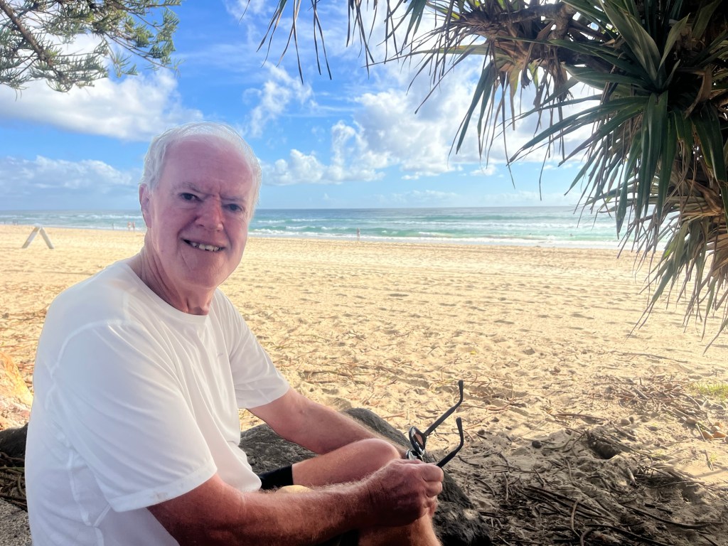 A picture of my husband Peter smiling with a beach view in the background - depicting the beautiful, humble man who is my husband